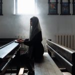 woman in black with scarf on head sitting on bench in church