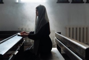 woman in black with scarf on head sitting on bench in church