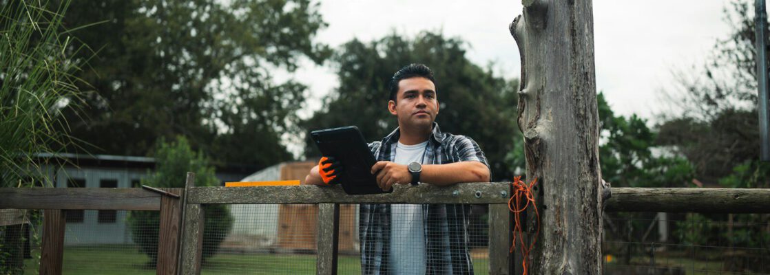Man holding tablet standing by a wooden fence outdoors