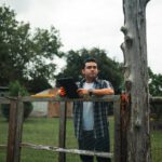 Man holding tablet standing by a wooden fence outdoors