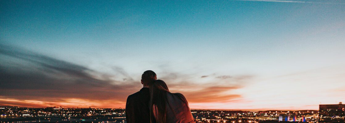 couple sitting on the field facing the city