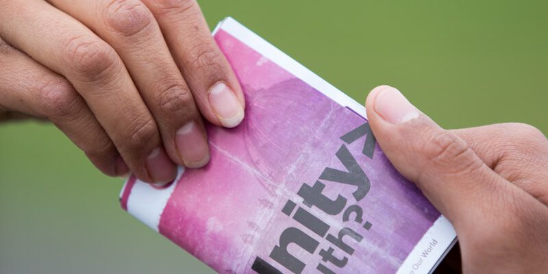 selective focus photography of two persons holding purple and white Unity truth? booklet